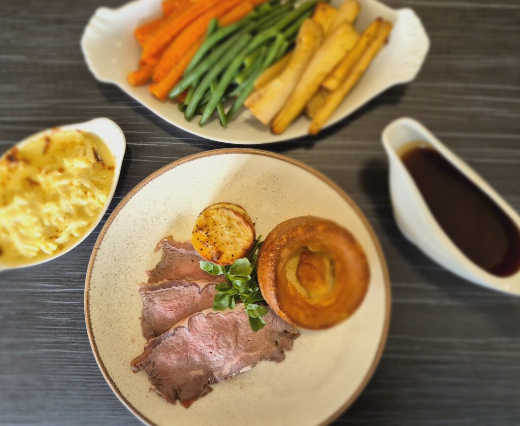 Sunday lunch with roast beef, potatoes, yorkshire pudding, cauliflower cheese, vegetables and gravy