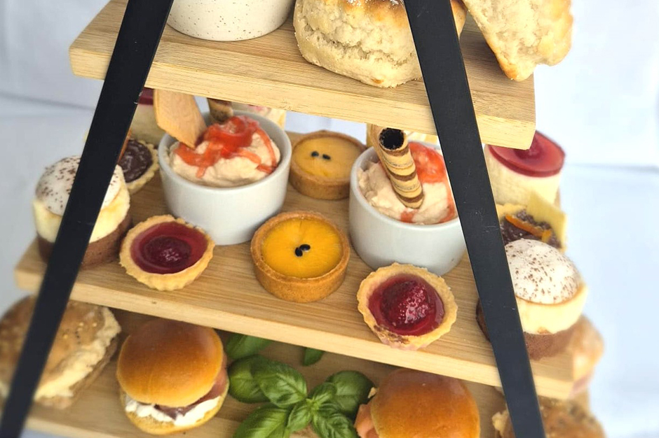 Close up of afternoon tea stand with filled rolls, sweet treats and freshly baked scones